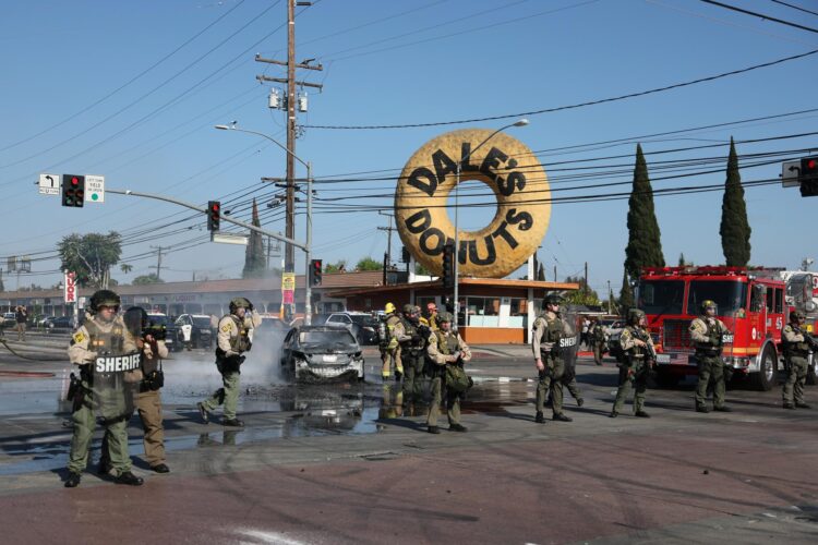 PARAMOUNT (United States), 07/06/2025.- Law enforcement stand in front of a burned car near a Home Depot after a raid was conducted by Immigration and Customs Enforcement (ICE) in Paramount, California, USA, 07 June 2025. This comes the day after federal immigration authorities arrested more than 40 people across Los Angeles, as protesters gathered outside a federal detention center. (Protestas) EFE/EPA/ALLISON DINNER